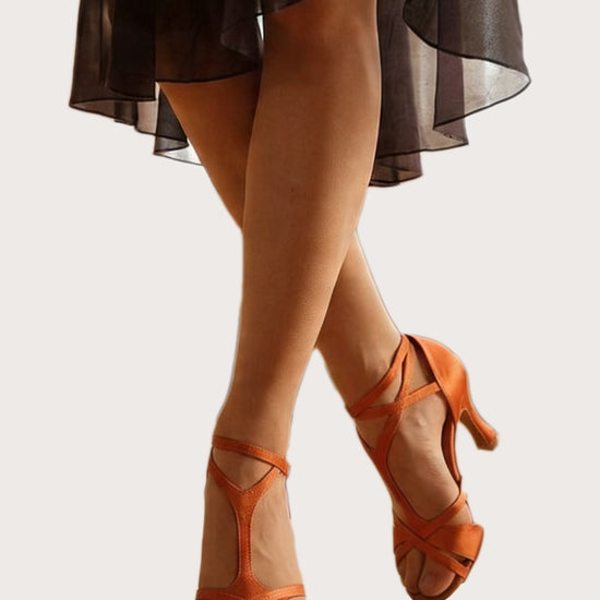 Orange Satin Latein‑Tanzschuhe mit überkreuzten Riemchen und 8‑cm Absatz an Tänzerbeinen vor hellem Hintergrund