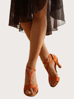 Orange Satin Latein‑Tanzschuhe mit überkreuzten Riemchen und 8‑cm Absatz an Tänzerbeinen vor hellem Hintergrund