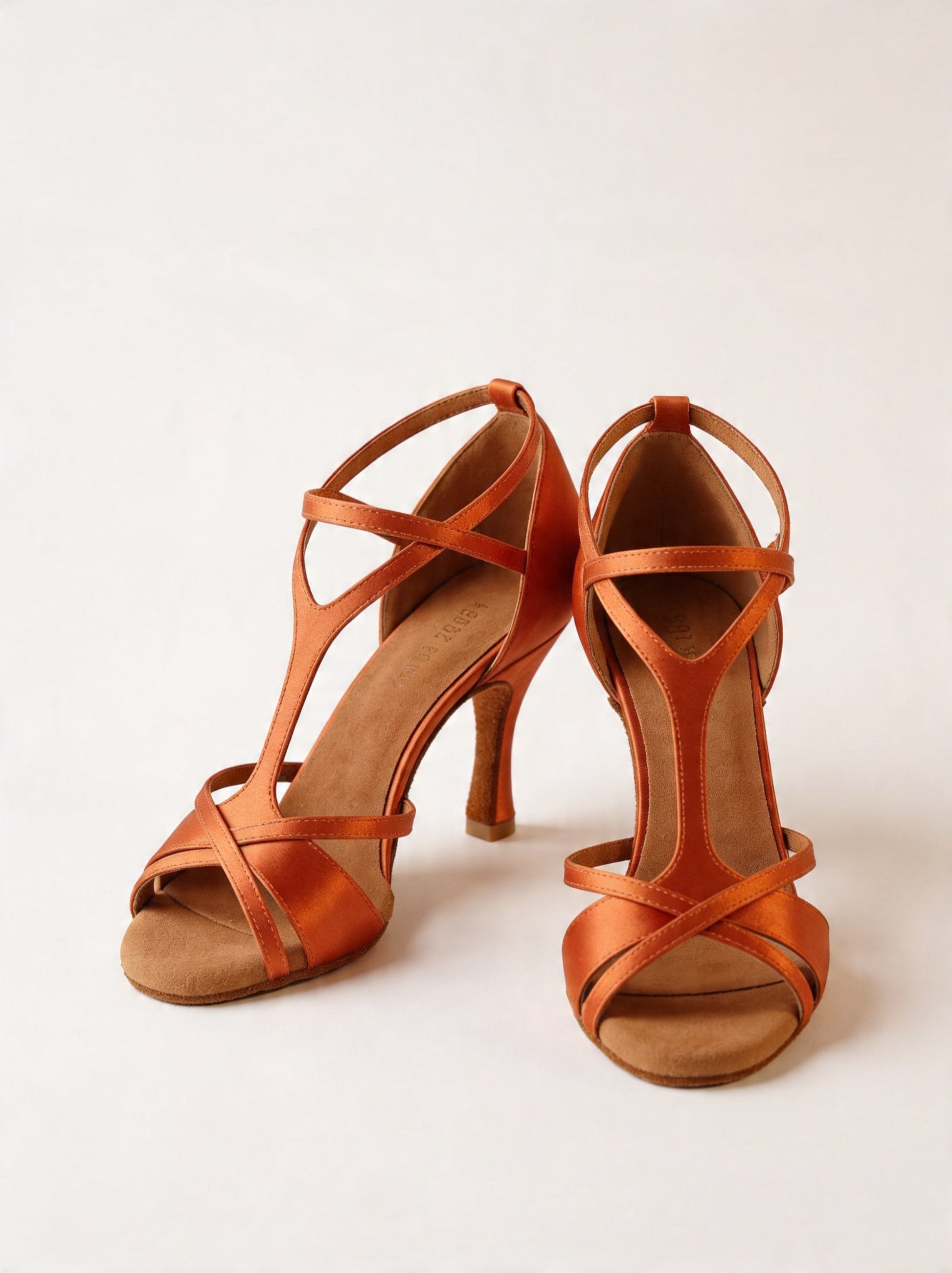 Orange Satin Latein‑Tanzschuhe mit überkreuzten Riemchen und 8‑cm Absatz an Tänzerbeinen vor hellem Hintergrund