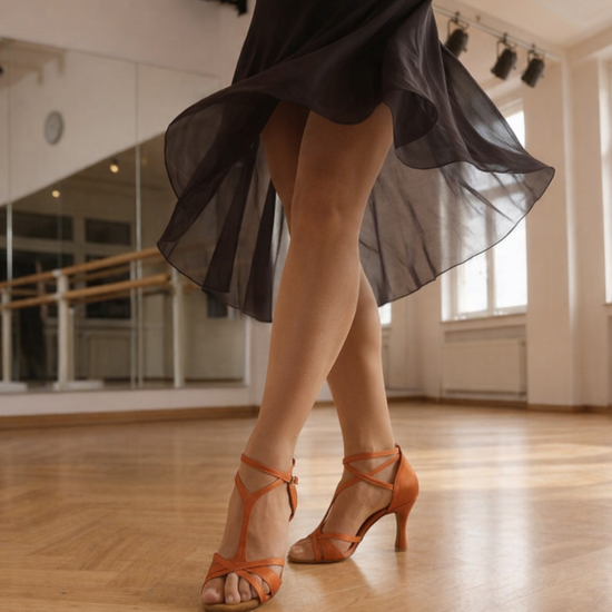 Orange Satin Latein‑Tanzschuhe mit überkreuzten Riemchen und 8‑cm Absatz an Tänzerbeinen vor hellem Hintergrund