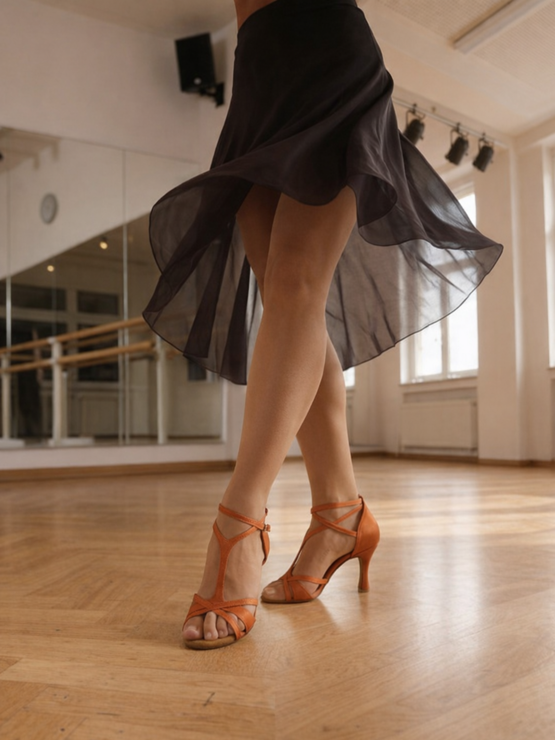 Orange Satin Latein‑Tanzschuhe mit überkreuzten Riemchen und 8‑cm Absatz an Tänzerbeinen vor hellem Hintergrund